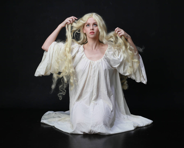 Strašidelný portrét ženy s dlouhými blond vlasy na bílém plášti. póza na černém studiovém pozadí.  - Fotografie, Obrázek
