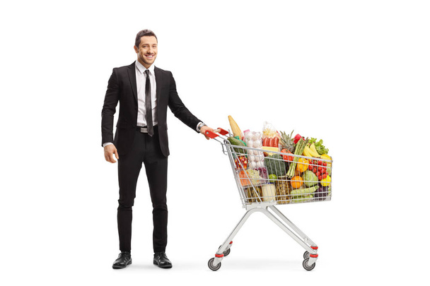 Businessman posing with a shopping cart with food - Zdjęcie, obraz