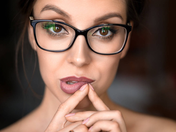 Portrait of a charming woman in eyeglasses smiling and touching her lips. Eyesight concept. Close up portrait - Photo, Image
