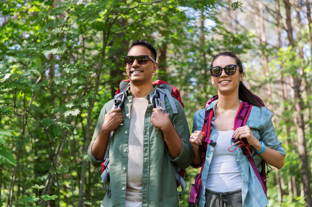 mixed race couple with backpacks hiking in forest - Fotó, kép