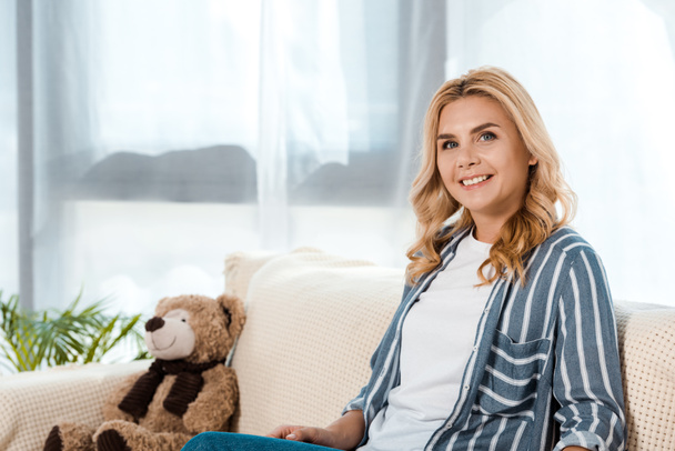 happy woman sitting on sofa near soft toy  - Fotografie, Obrázek