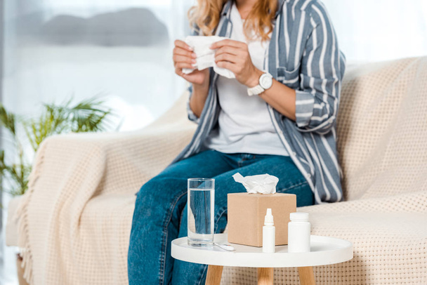 vue recadrée de la femme assise sur le canapé et tenant une serviette près du verre avec de l'eau
  - Photo, image