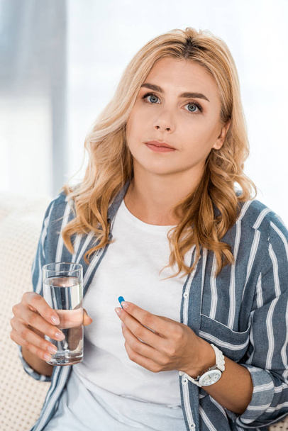 woman looking at camera while holding glass with water and pill  - Фото, зображення