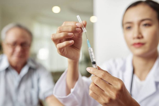 Nahaufnahme einer jungen Ärztin mit Spritze, die im Hintergrund im Krankenhaus eine Impfung für die Patientin macht - Foto, Bild