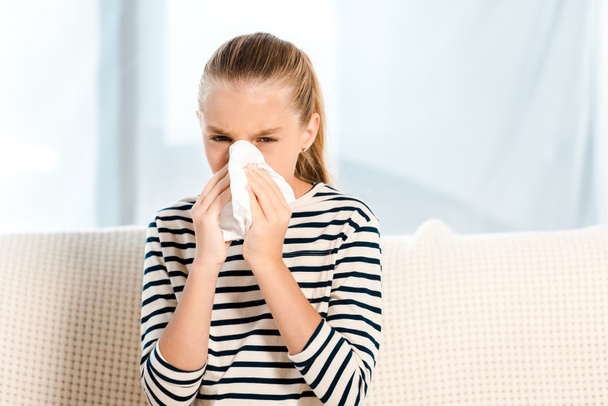 diseased kid sneezing in tissue and looking at camera  - Photo, image