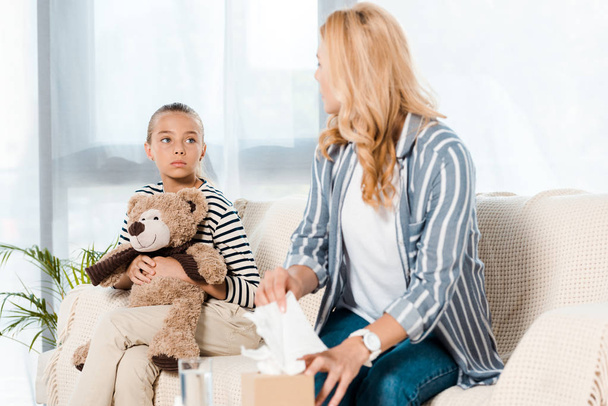 niño con oso de peluche mirando a la madre enferma tomando tejido en casa
  - Foto, Imagen