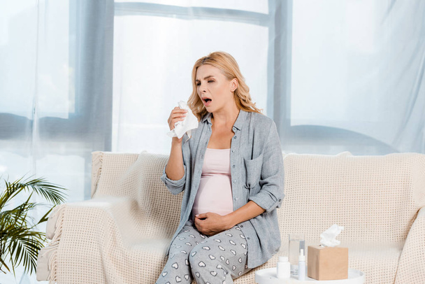 sick pregnant woman touching belly wile sneezing at home  - Photo, Image
