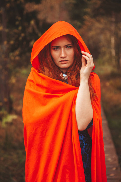 Pretty Red Riding Hood Woman is going on autumn forest road. - Foto, Bild