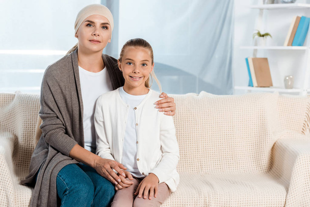 Kranke Mutter sitzt mit glücklicher Tochter auf Sofa  - Foto, Bild