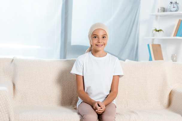 happy kid in head scarf sitting on sofa in living room  - Photo, Image