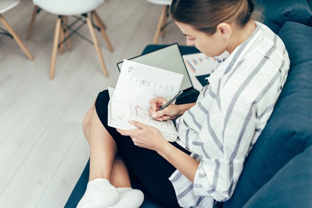 Mujer joven adulta escribiendo en la agenda, trabajando en la oficina en casa
 - Foto, Imagen