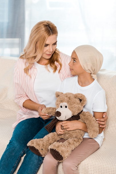 attractive mother sitting on sofa with sick kid with teddy bear  - Фото, зображення