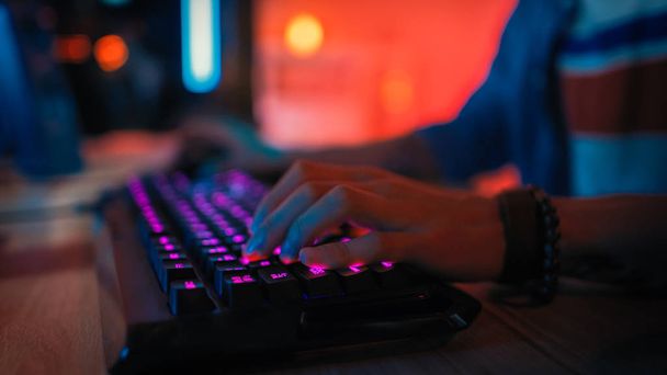 Close Up Hands Shot Mostrando um jogador Empurrando os botões do teclado enquanto joga um jogo de vídeo online. Teclado levou luzes. Gamer está usando uma pulseira. O quarto é escuro
. - Foto, Imagem