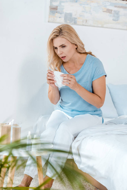 selective focus of woman holding cup with tea while sitting on bed  - Photo, Image