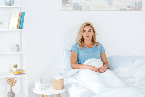 upset woman lying in bed near table with tissue box  - Foto, afbeelding