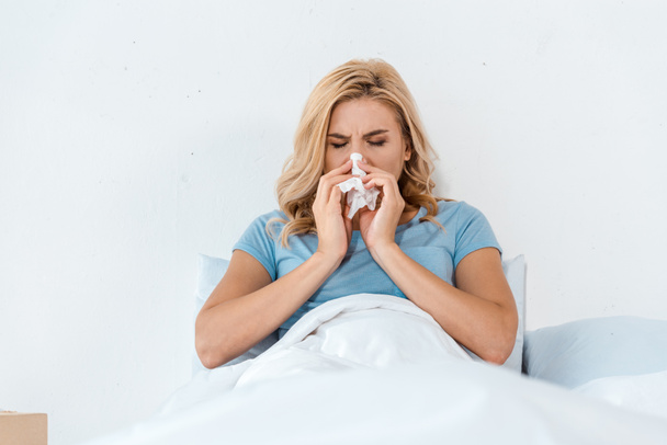 sick woman sneezing in napkin while lying in bed  - Photo, Image