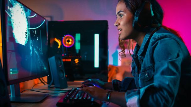 Pretty and Excited Black Gamer Girl in Headphones is Playing First-Person Shooter Online Video Game on Her Computer. Room and PC have Colorful Neon Led Lights. Cozy Evening at Home. - Photo, Image
