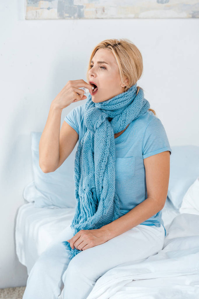 sick woman in scarf taking pill while sitting on bed - Fotografie, Obrázek