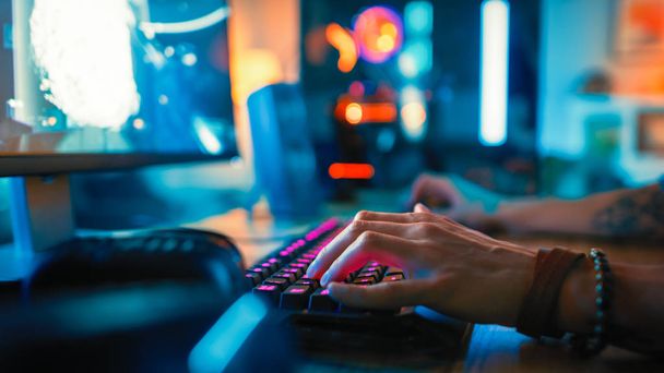 Close-Up Hands Shot Showing a Gamer Using the Keyboard while Playing an Online Shooter Video Game. Keyboard has Pink Neon Lights in Buttons. Gamer is Wearing a Bracelet. Room is Dark. - Foto, imagen