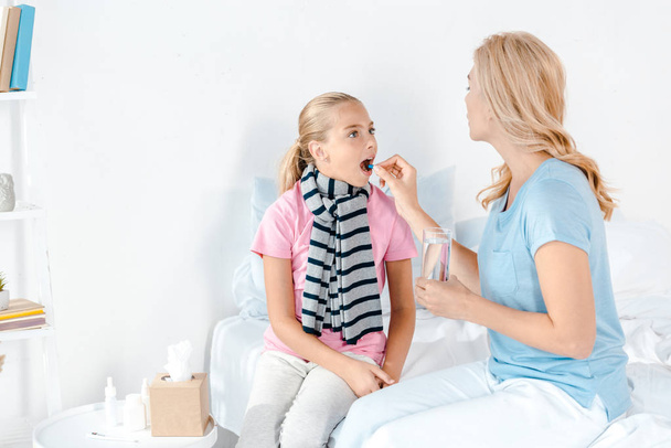 madre dando píldora a hija enferma con la boca abierta
  - Foto, imagen