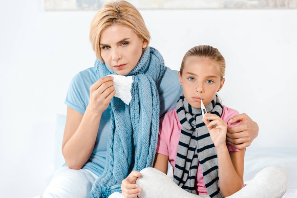 sick mother holding tissue near ill kid with digital thermometer  - Photo, Image