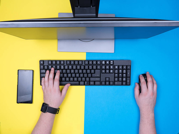 Mavi ve sarı arka plan üzerinde bir bilgisayar klavyesi üzerinde yazarak adam düz yatıyordu - Fotoğraf, Görsel