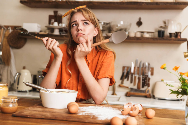 Sad young blonde girl chef cooking at the kitchen thinking. - Φωτογραφία, εικόνα