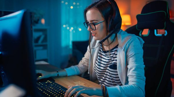 Excited Gamer Girl in Headset with a Mic Playing Online Video Game on Her Personal Computer. She Talks to Other Players. Room and PC have Colorful Warm Neon Led Lights. Cozy Evening at Home. - Photo, Image