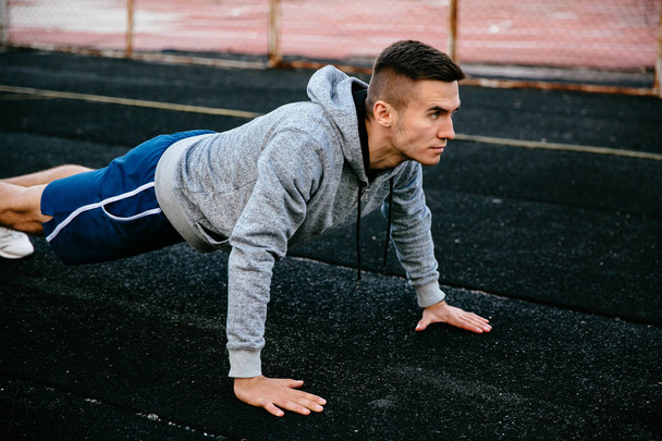 Sportsman faisant de l'exercice de planche sur un terrain d'athlétisme
 - Photo, image