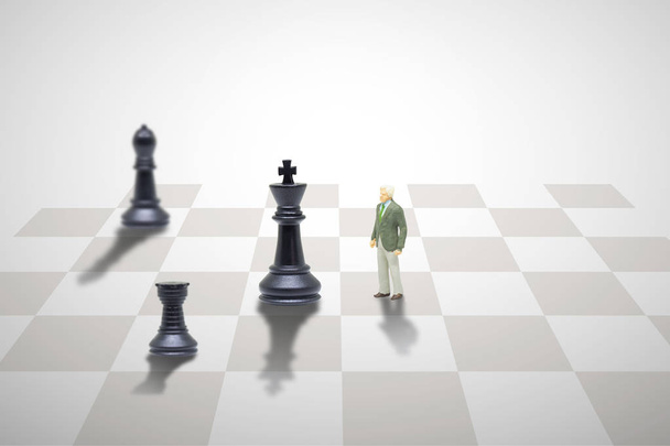 Έννοια του επιχειρηματικού ανταγωνισμού: μινιατούρα χαρακτήρα αγαλματάκι ως επιχειρηματίας που στέκεται πρόσωπο με πρόσωπο με το βασιλικό κομμάτι σκακιού στη σκακιέρα. - Φωτογραφία, εικόνα