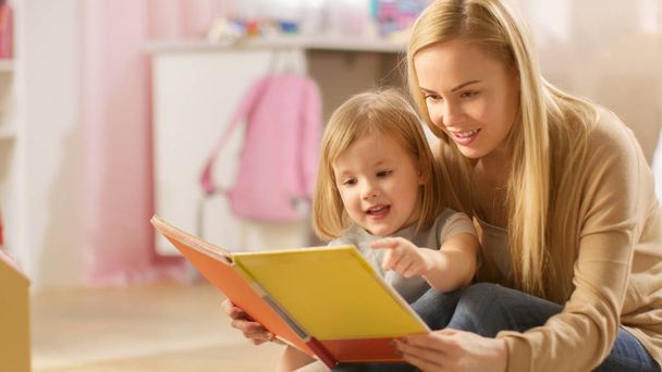 Beautiful Young Mother and Her Cute Little Daughter Read Children's Book Together. Children's Room is Pink and Full of Toys. - Foto, Imagen