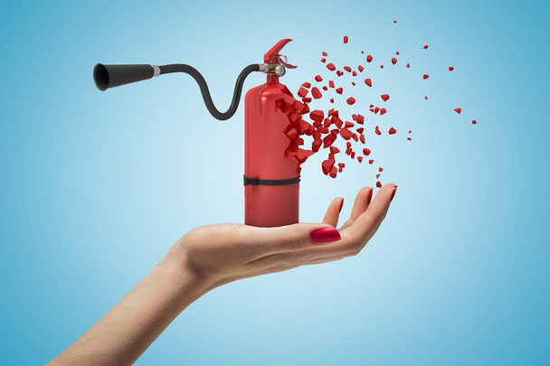 Female hand holding red fire extinguisher shattering into pieces on blue background - Фото, зображення