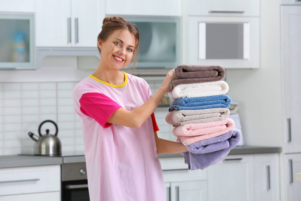 Happy young woman holding clean laundry in kitchen - Фото, зображення
