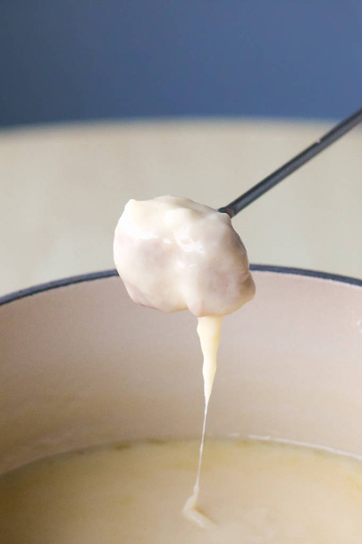スイスの伝統的な料理 - チーズフォンデュ。フォンデュフォークのバゲットは溶けたチーズに浸されています。キャンドルまたはスピリットランプで加熱された共用ポットで提供しています。写真をクローズアップします。縦の写真 - 写真・画像