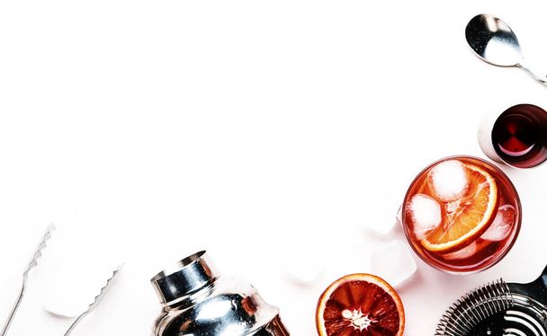 Negroni alcoholic cocktail with dry gin, red vermouth and red bitter, bloody orange slice and ice cubes. White background, steel bar tools, top view, copy space - Foto, Imagen
