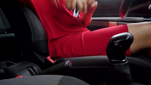 Žena v červených šatech utahování bezpečnostního pásu auta při sezení uvnitř vozidla před autem - Záběry, video