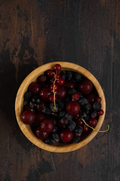 Ripe black and red currants in a wooden bowl on a wooden table. Organic food, berries, harvest season. - Photo, image