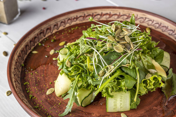 Вегетарианский полезный зеленый салат с авокадо, огурцом, рукколой и микро-зеленым, приправленный оливковым маслом на светлом фоне, горизонтальная ориентация
 - Фото, изображение