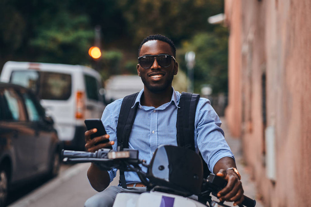 Young black man on scooter with mobile phone - 写真・画像