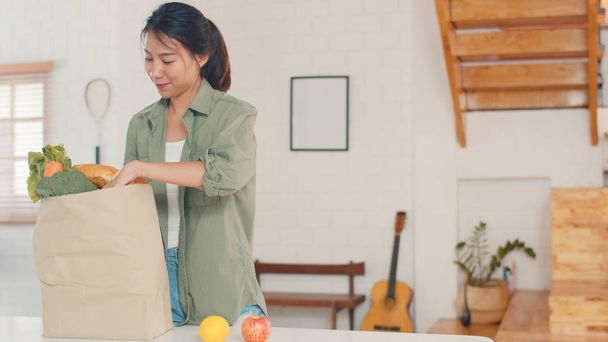 Азиатские женщины, держащие продуктовый магазин бумажные пакеты дома, молодая азиатка счастлива купить овощи и фрукты здоровый и органический продукт из супермаркета положить его на кухню в утренней концепции
. - Фото, изображение