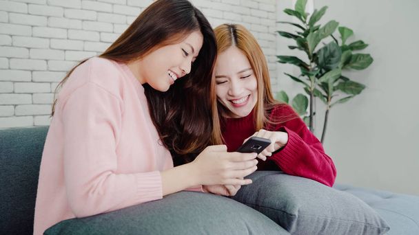 Asian women using smartphone checking social media in living room at home, group of roommate friend enjoy funny moment while lying on the sofa. Lifestyle women relax at home concept. - Фото, изображение