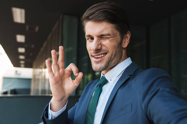 Photo of successful businessman showing ok sign and taking selfi - Zdjęcie, obraz