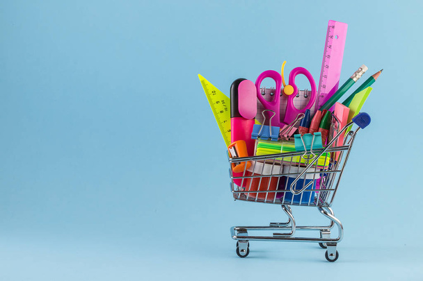 Shopping cart with different stationery on the blue background. - Photo, Image