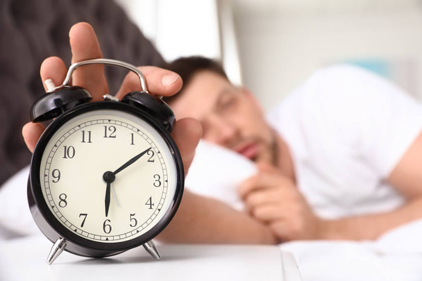 Sleepy man turning off alarm clock on nightstand. Bedtime - Valokuva, kuva