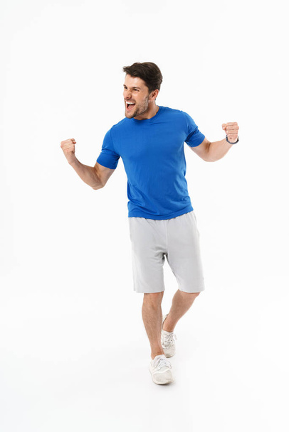 Full length photo of joyful man in shorts and t-shirt screaming and rejoicing with clenching fists - Foto, afbeelding
