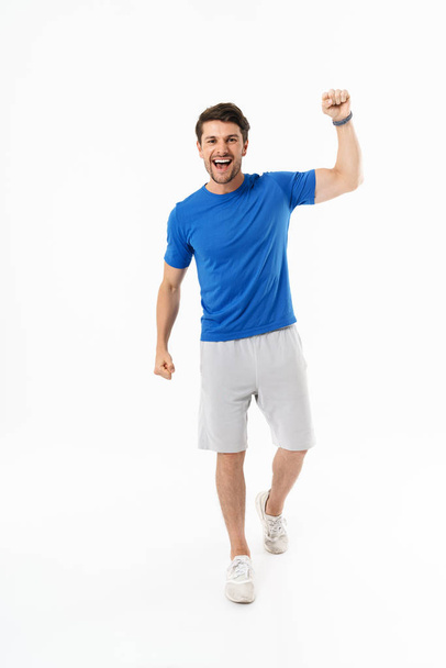 Full length photo of young man in shorts and t-shirt screaming and rejoicing with clenching fist - Zdjęcie, obraz
