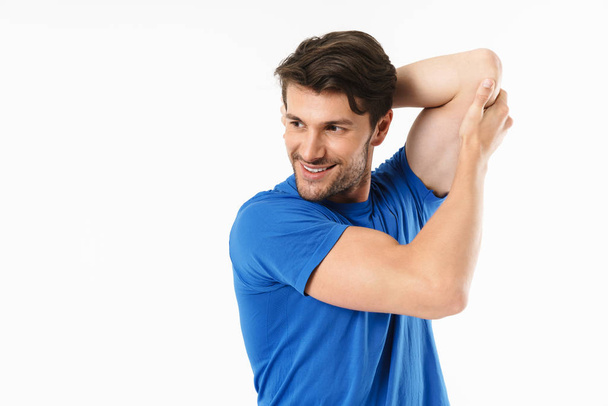 Cheerful young sports fitness man standing isolated over white wall background make stretching exercises for arms triceps. - Φωτογραφία, εικόνα