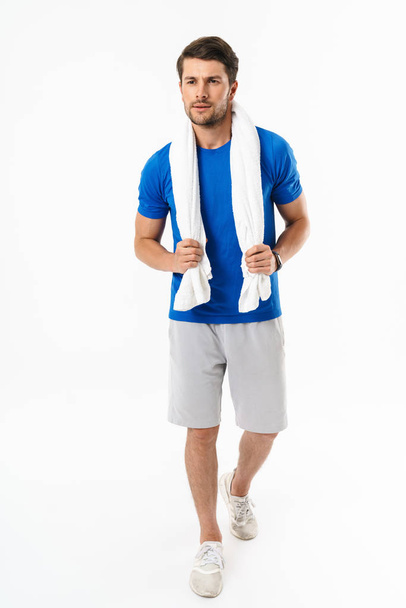 Handsome young sports fitness man standing isolated over white wall background holding towel. - Zdjęcie, obraz