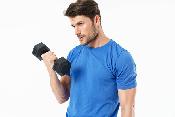 Serious handsome young sports fitness man standing isolated over white wall background holding dumbbells. - Фото, зображення