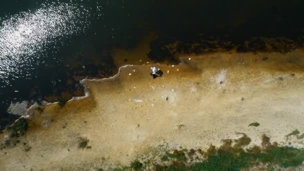 保護スーツを着た男と、乾燥した汚染された川のほとりにプラスチックゴミを集める人工呼吸器の空中写真。生態学的な大きなトロフィー人為的影響4Kドローン映像. - 映像、動画